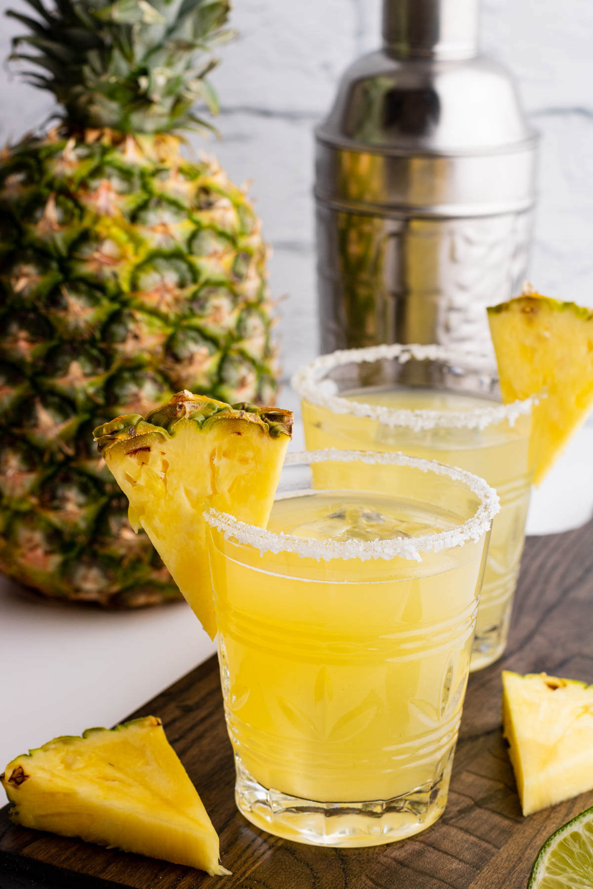 Two rimmed rocks glasses filled with ice and pineapple margarita. Garnished with a slice of pineapple.