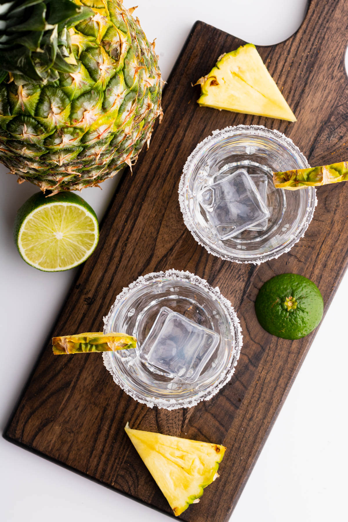 Two empty rimmed rocks glasses filled with ice and garnished with a slice of pineapple.