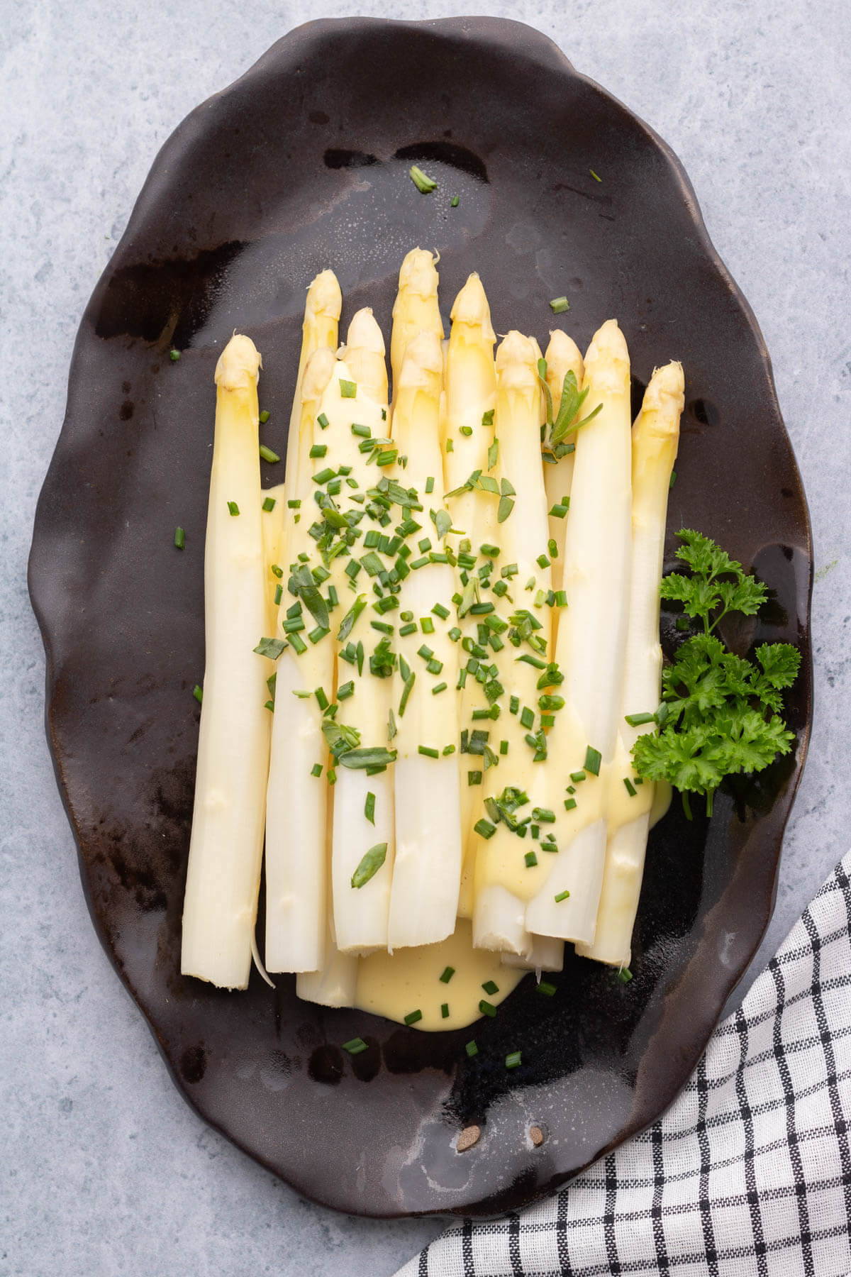 Steamed white asparagus covered in pale yellow hollandaise and green herbs. 