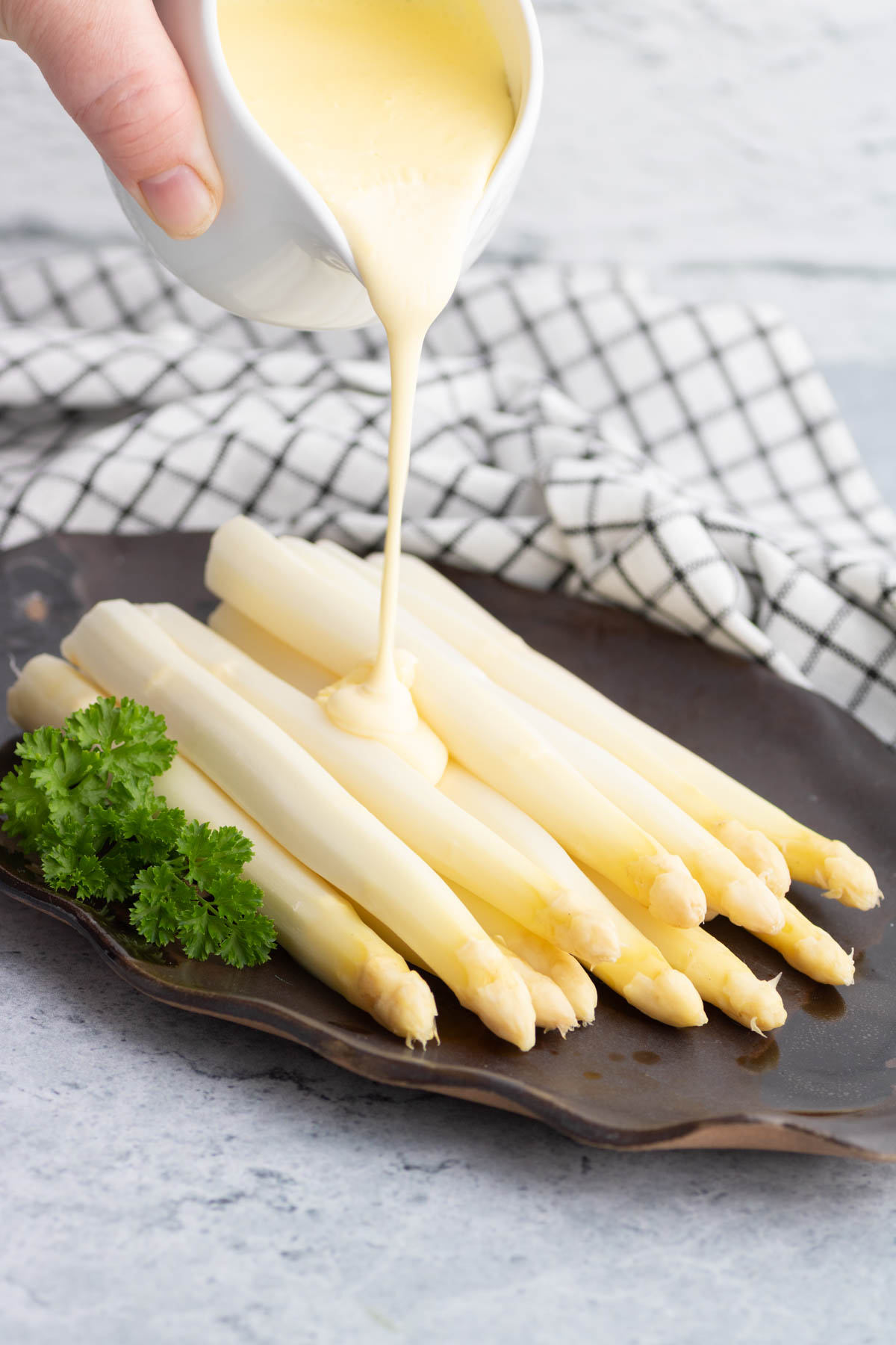 Light yellow Hollandaise sauce being poured on a bunch of steamed white asparagus.