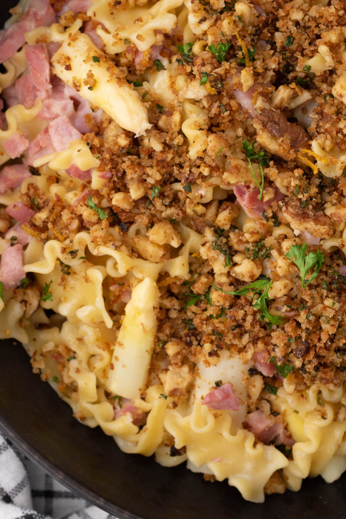 Close up of lemon butter pasta with ham and white asparagus topped with golden herbed bread crumbs.