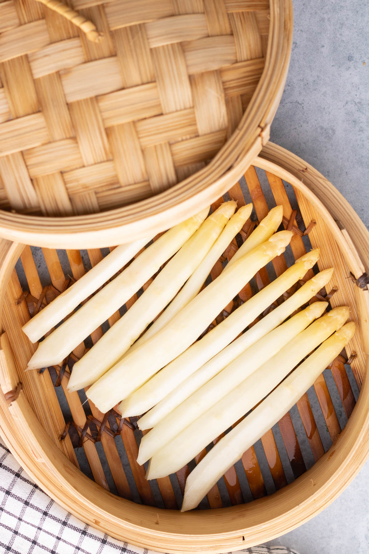 Peeled white asparagus in a bamboo steamer basket.