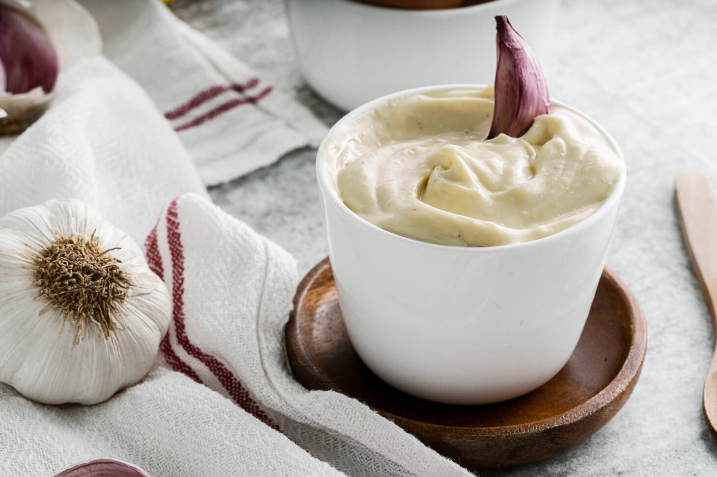 A small white dish filled with creamy Homemade Aioli garnished with a purple clove of garlic.