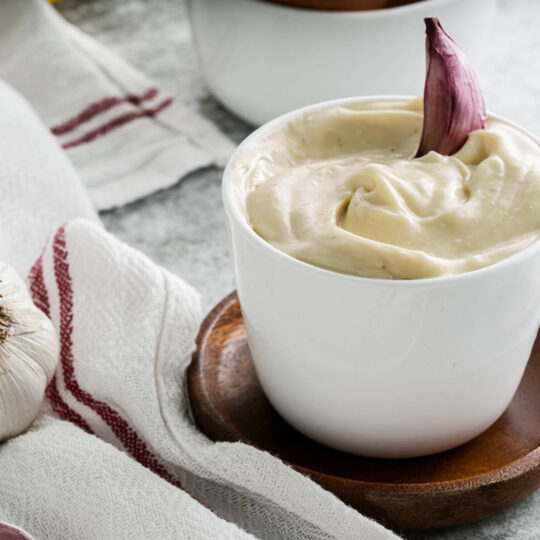 A small white dish filled with creamy Homemade Aioli garnished with a purple clove of garlic.