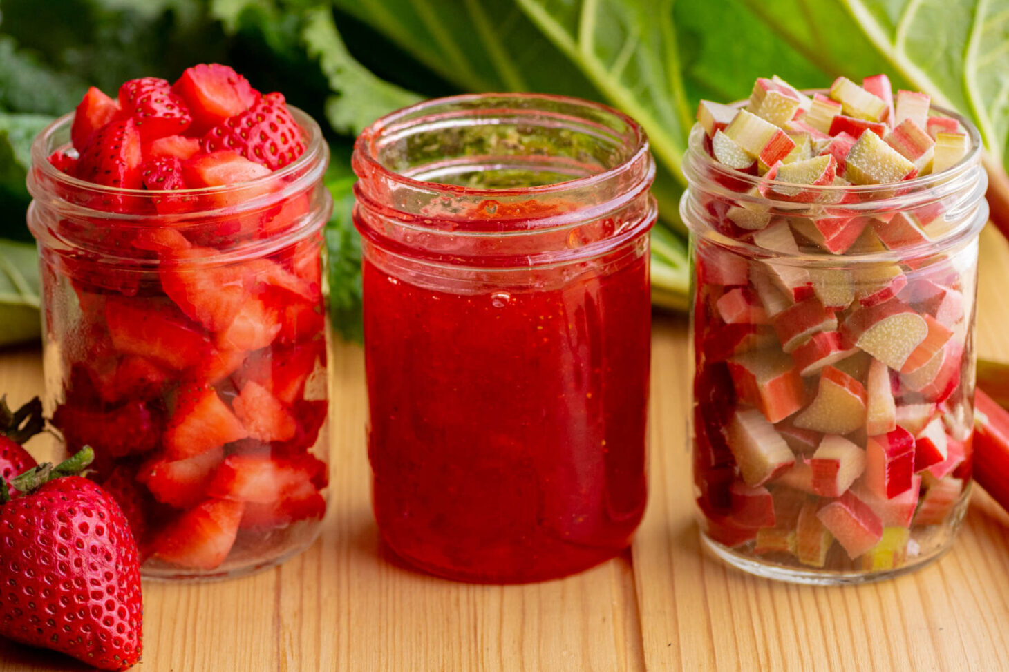 Three glass jars containing chopped strawberries, chopped rhubarb and strawberry rhubarb jam.
