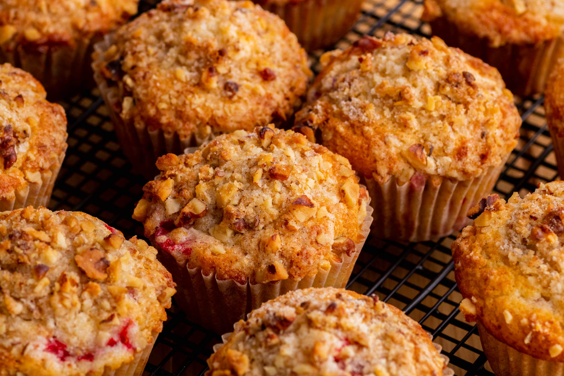 Golden baked strawberry rhubarb muffins cooling on a black round rack.