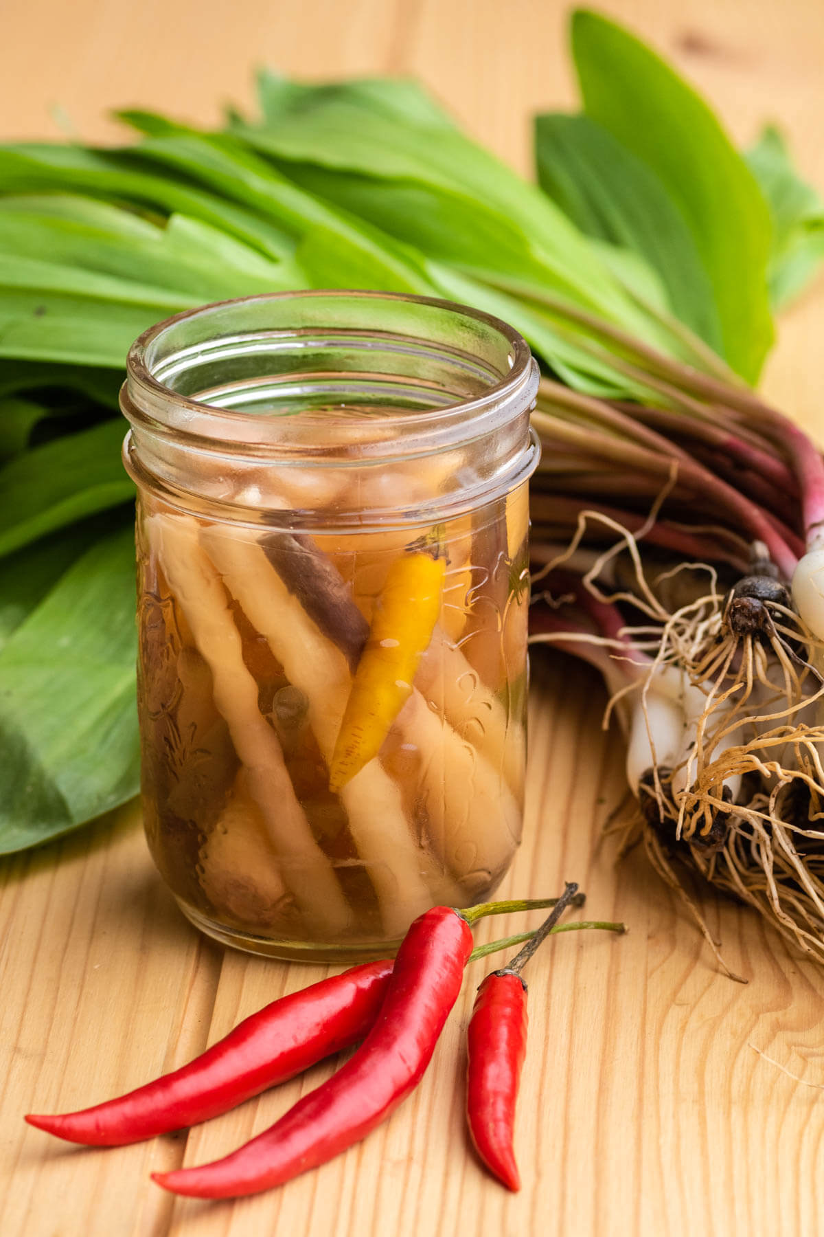 A jar of pickled ramps with fresh ramps and red Thai chilis.