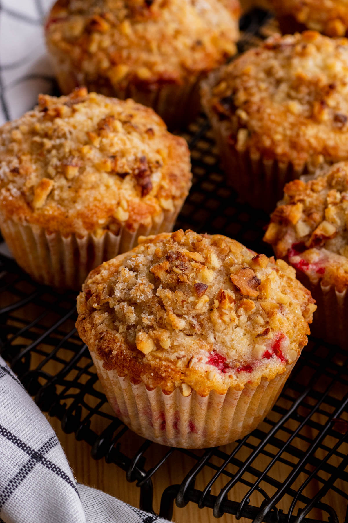 Golden baked strawberry rhubarb muffins cooling on a black round rack.