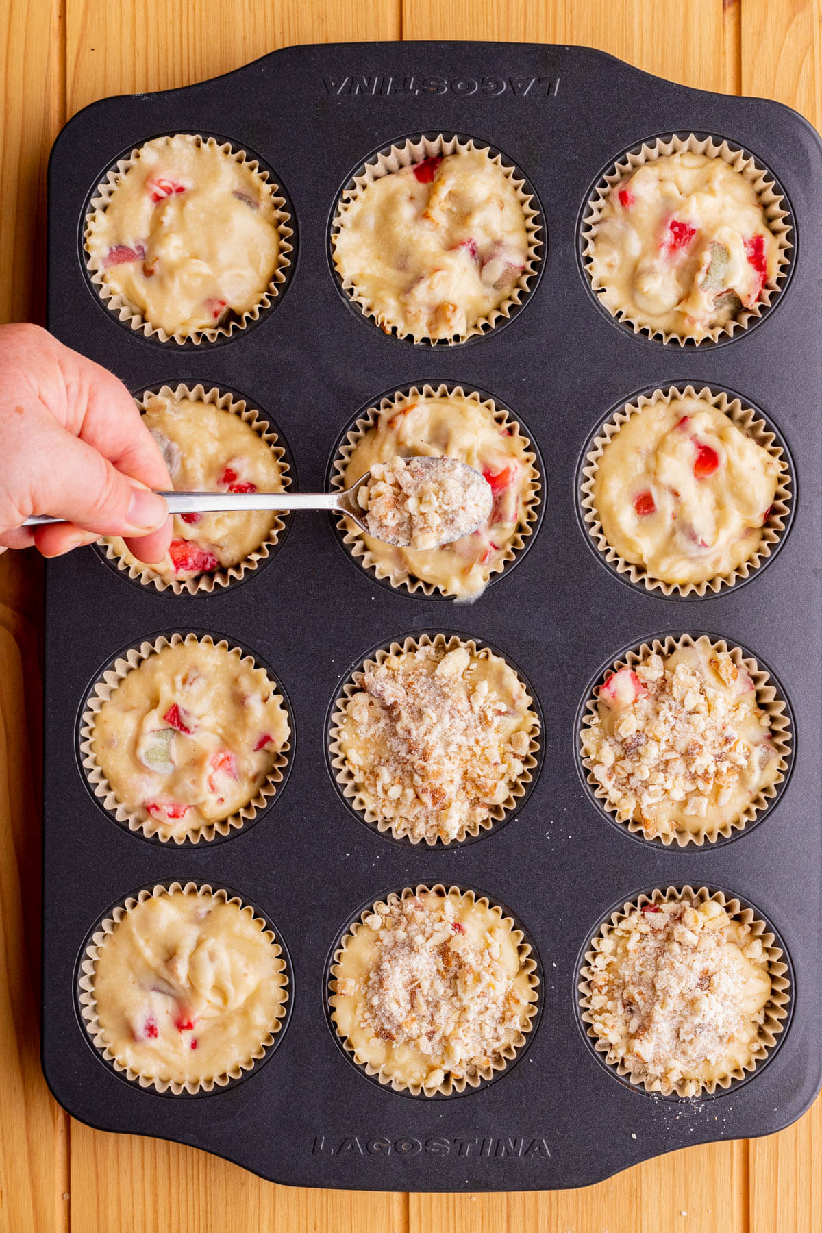 A spoon sprinkles streusel on unbaked strawberry rhubarb muffin batter.