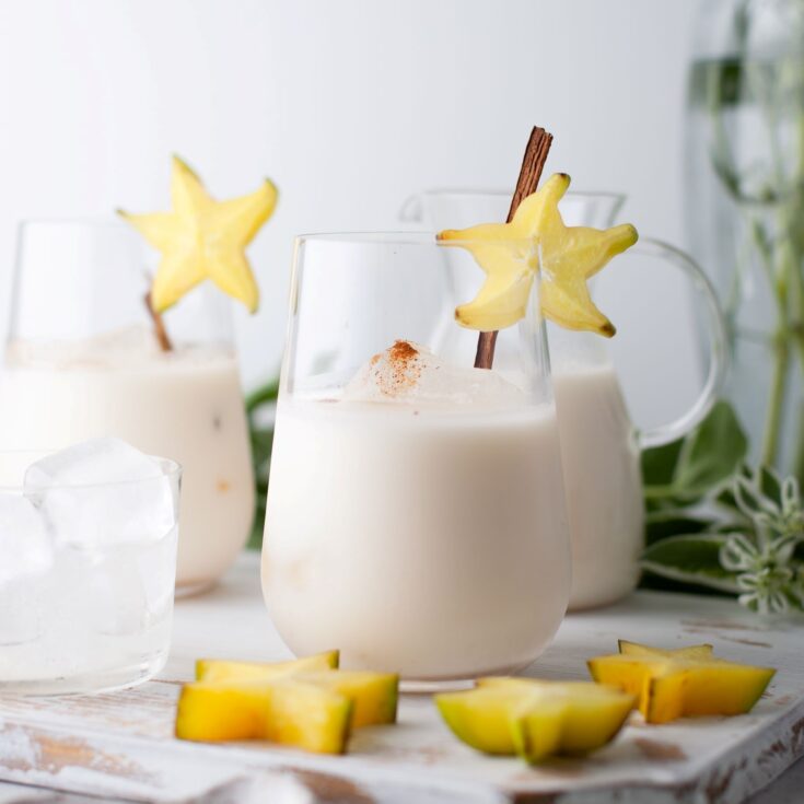 Glasses filled with creamy homemade horchata garnished with a cinnamon stick and starfruit.