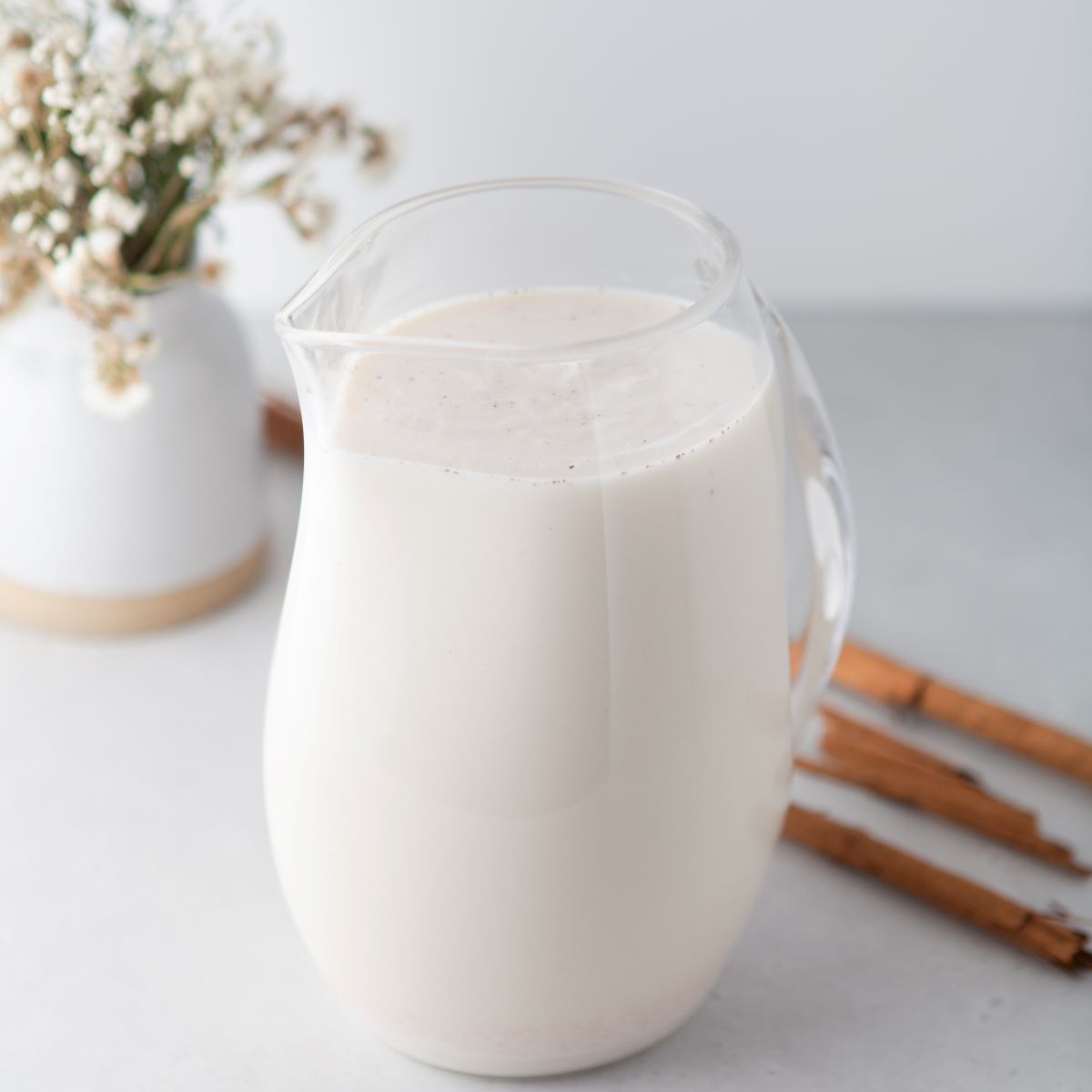 A glass pitcher filled with creamy homemade horchata surrounded by cinnamon sticks.