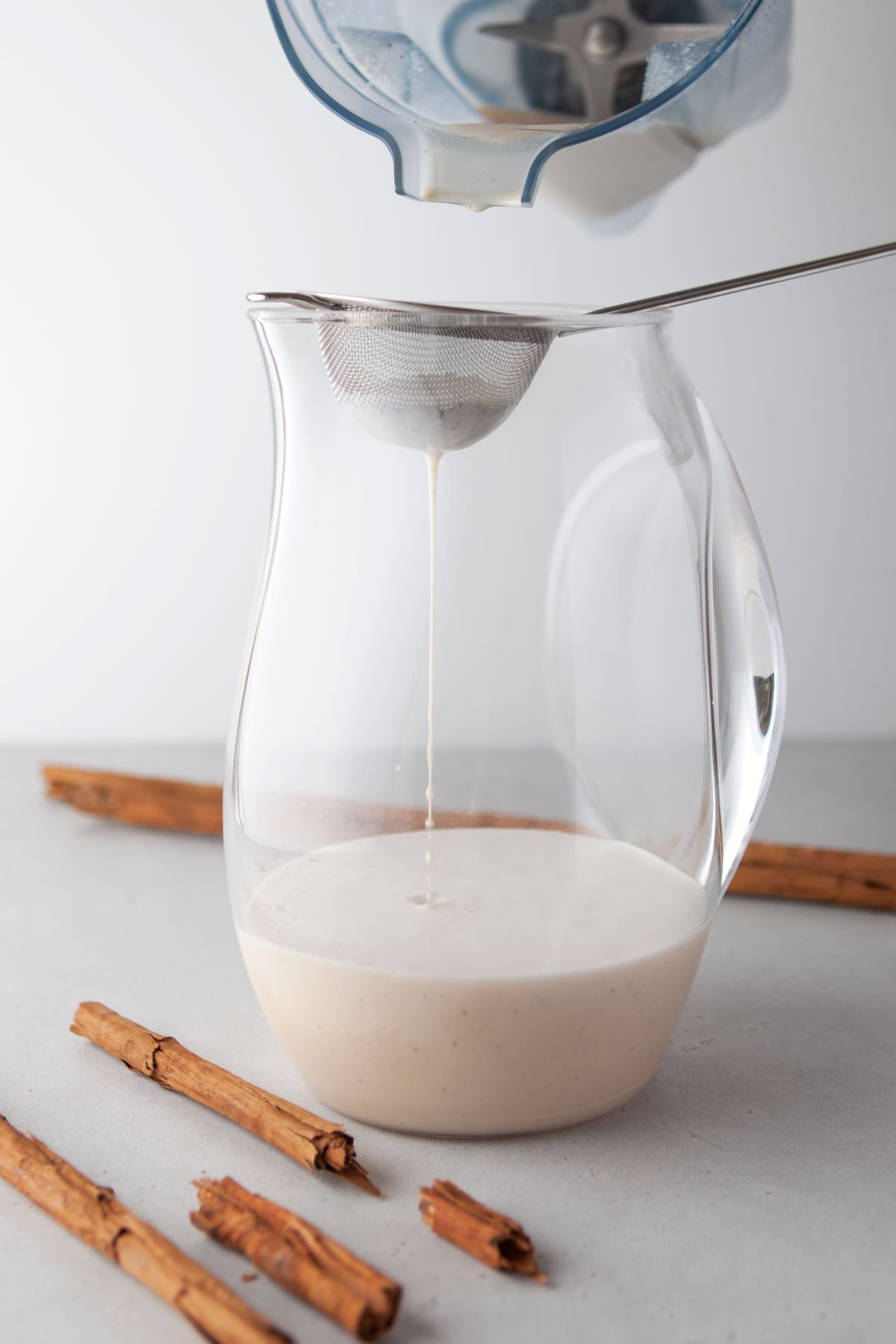 Blended horchata mixture being strained through a mesh strainer into a glass pitcher.