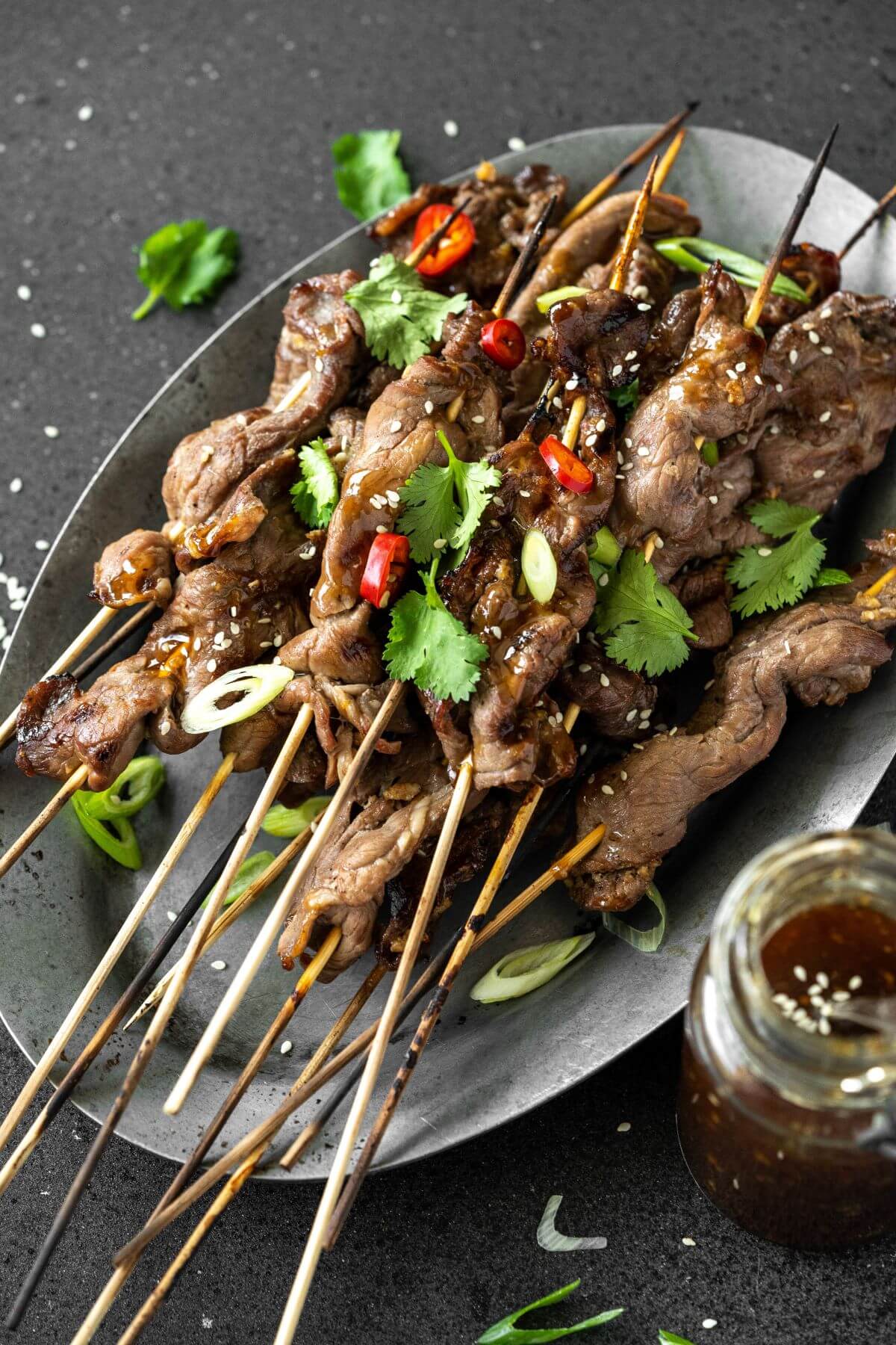 A platter of grilled Teriyaki Beef Sticks garnished with chopped green herbs and red hot peppers.