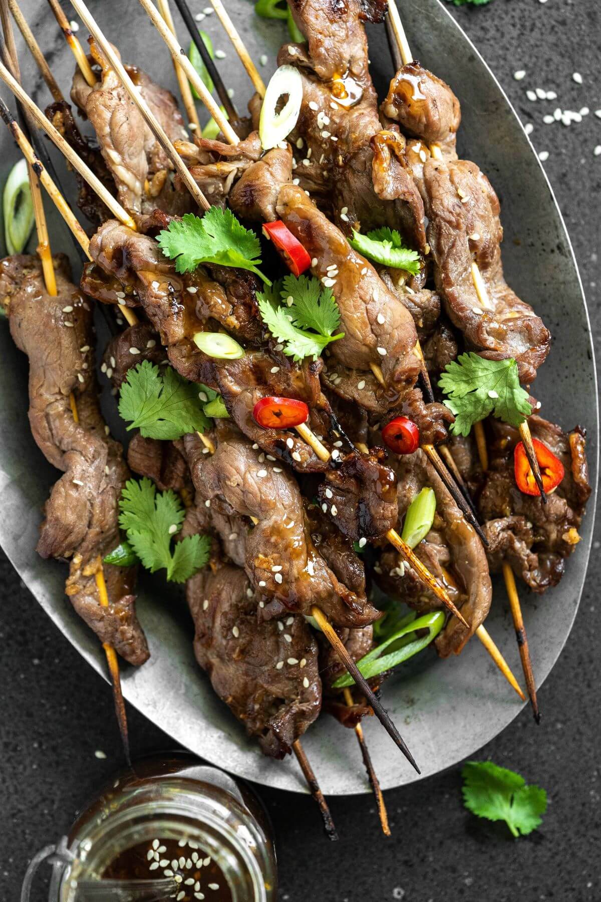 A platter of grilled Teriyaki Beef Sticks garnished with chopped green herbs and red hot peppers.