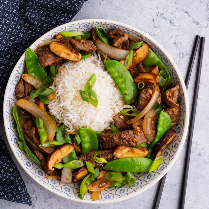 A bowl filled with beef stir fry and snow peas, white rice, shiitake mushrooms.