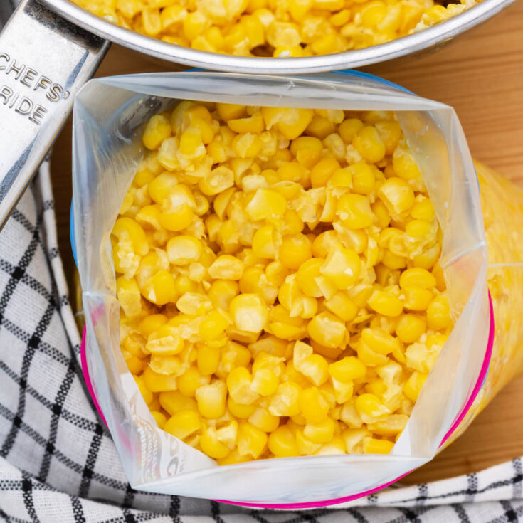 A freezer bag full of bright yellow corn kernels beside a saucepan of corn.