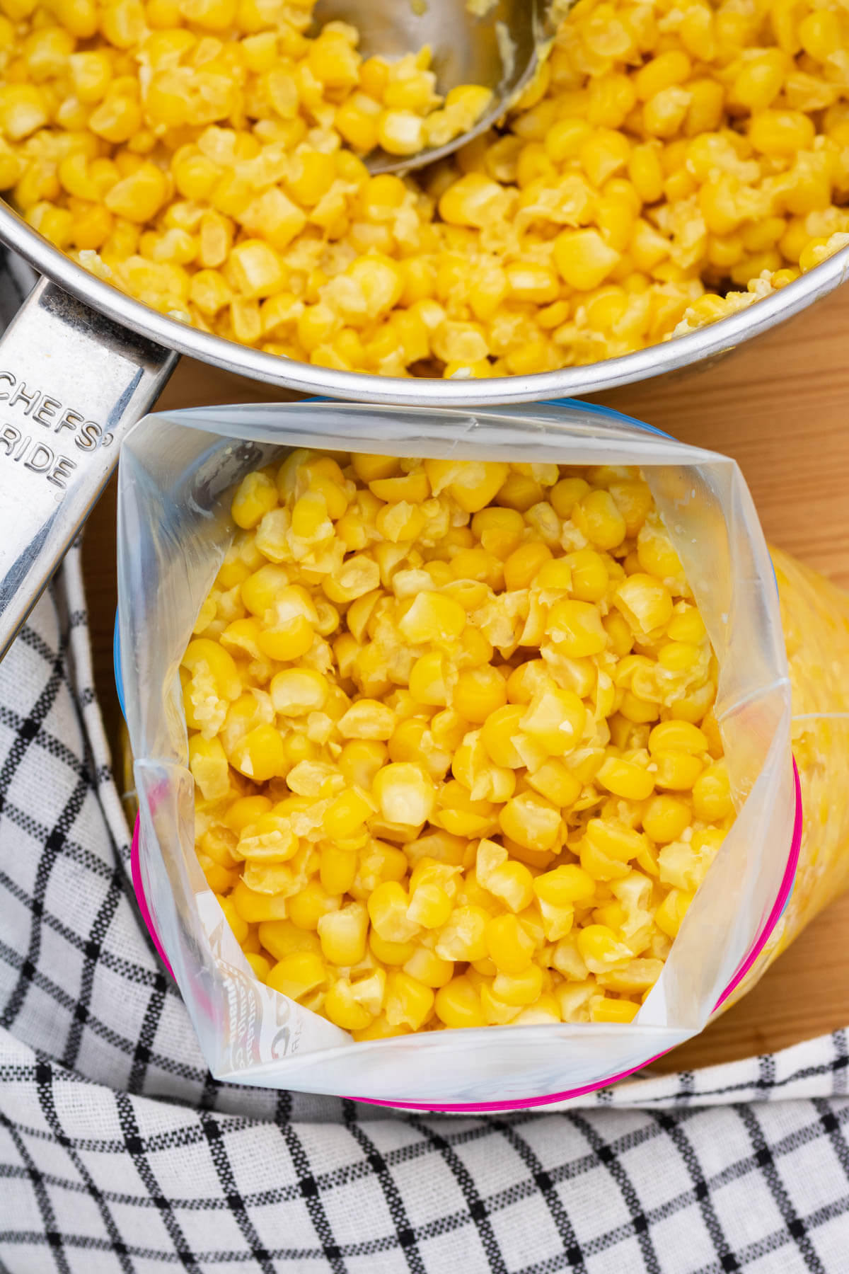 A freezer bag full of bright yellow corn kernels beside a saucepan of corn.