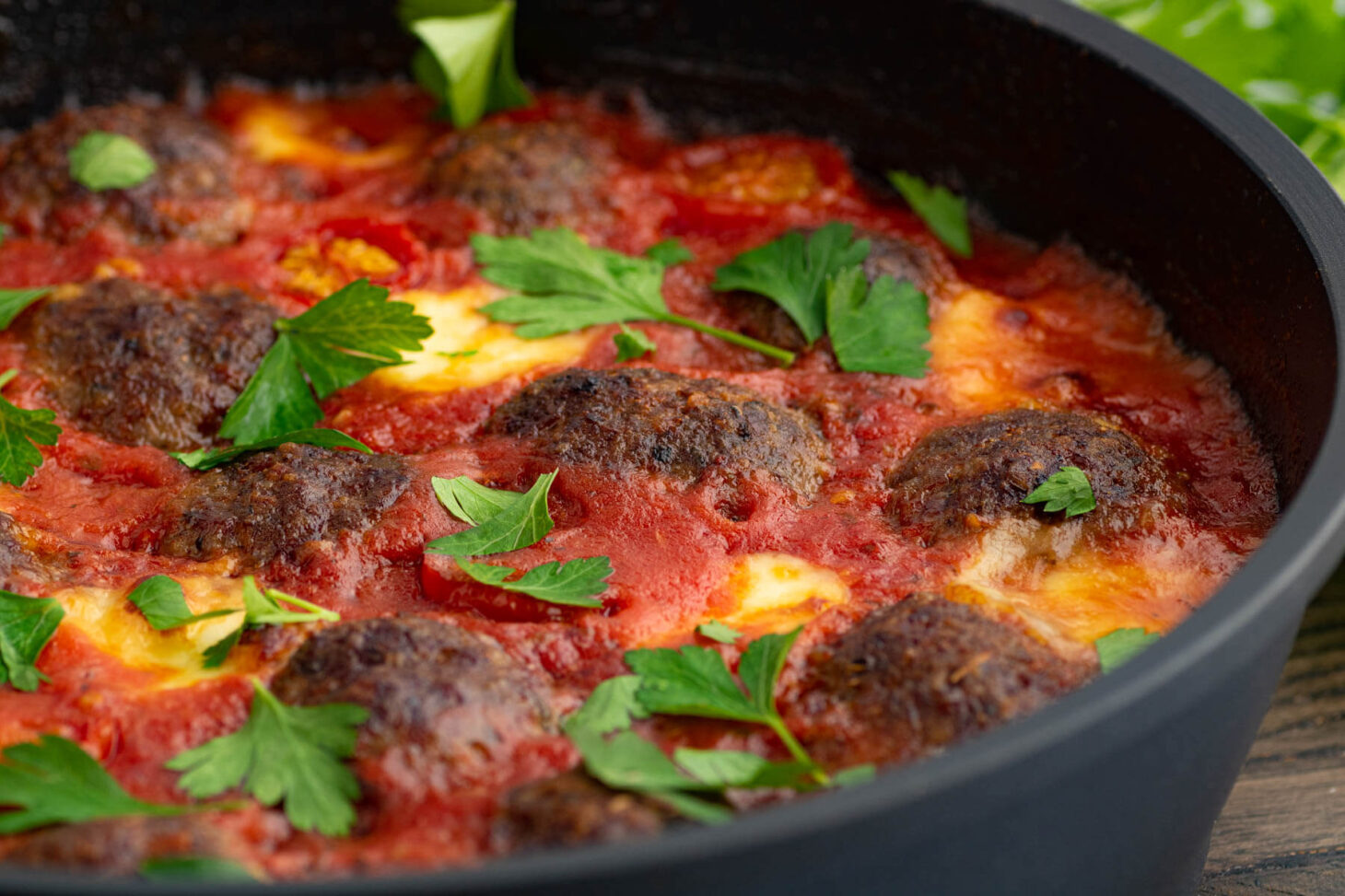A pan of Oven Baked Meatballs in a rich tomato sauce with melted cheese garnished with Italian parsley.