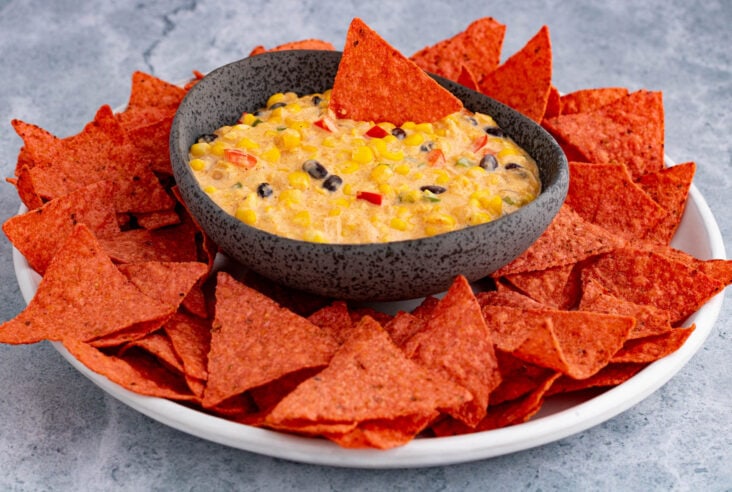 A stone bowl filled with sweet yellow Tex Mex Corn Dip surrounded by red tortilla chips.