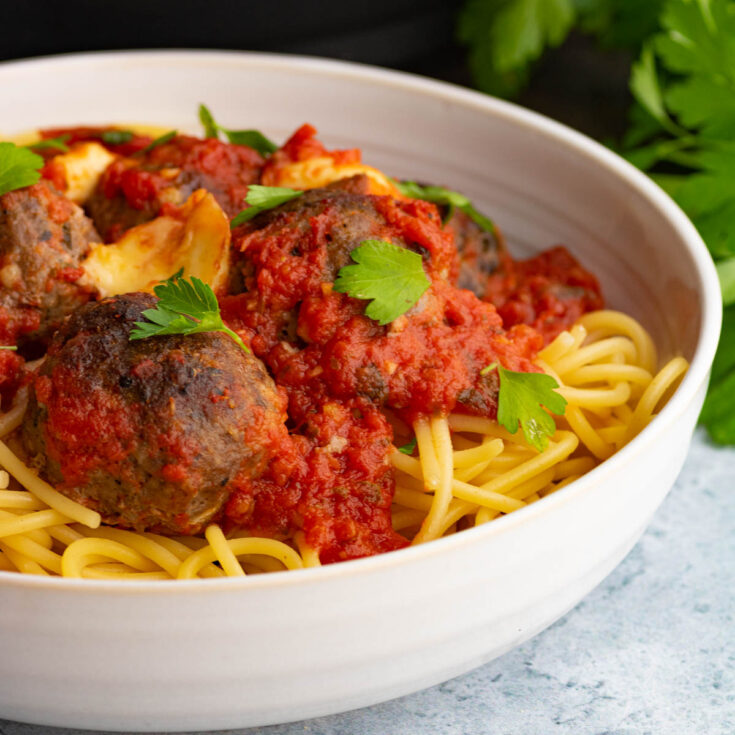 A bowl of spaghetti topped with rich tomato sauce, oven baked meatballs, and Italian parsley to garnish.