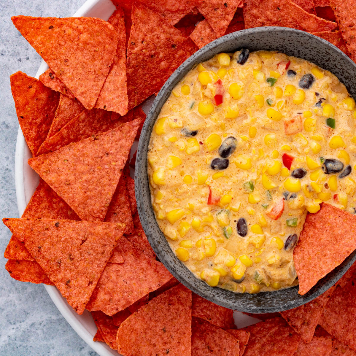 A stone bowl filled with sweet yellow Tex Mex Corn Dip surrounded by red tortilla chips.