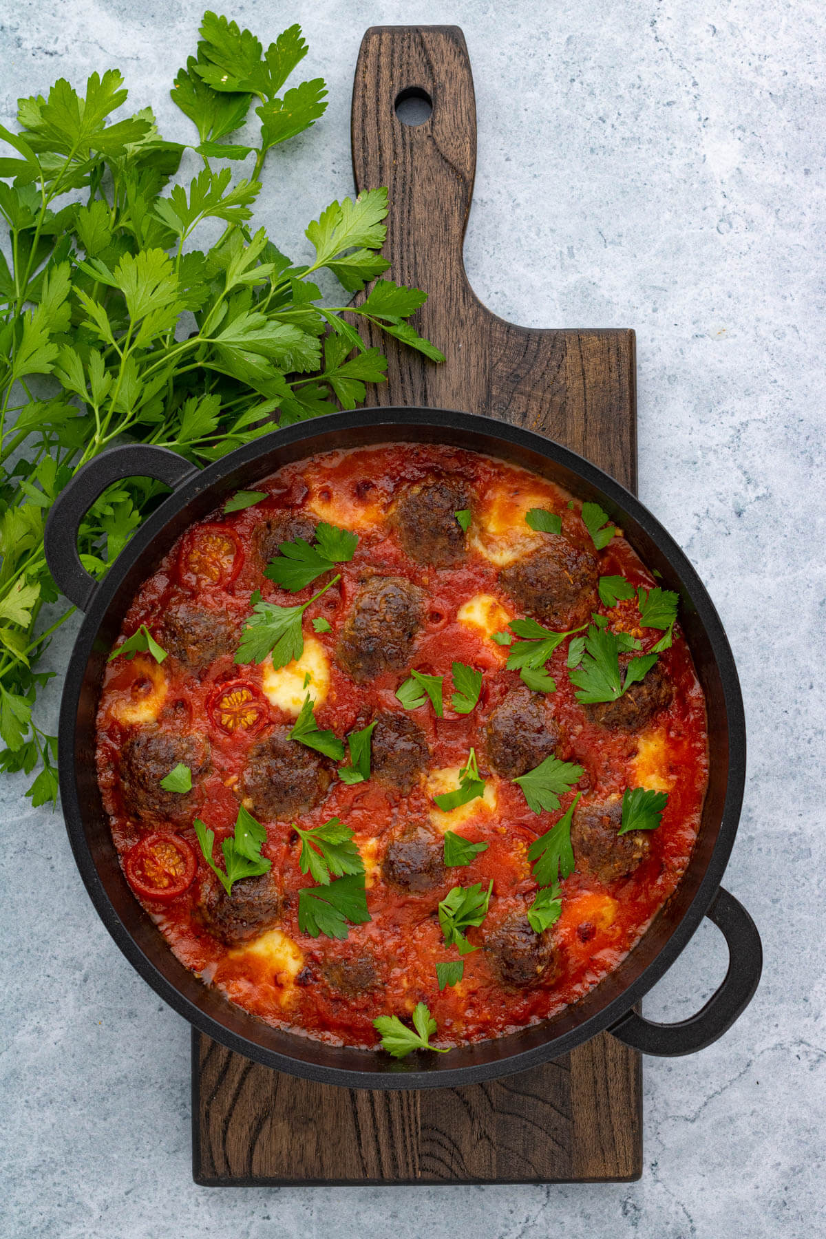 A pan of Oven Baked Meatballs in a rich tomato sauce with melted cheese garnished with Italian parsley.