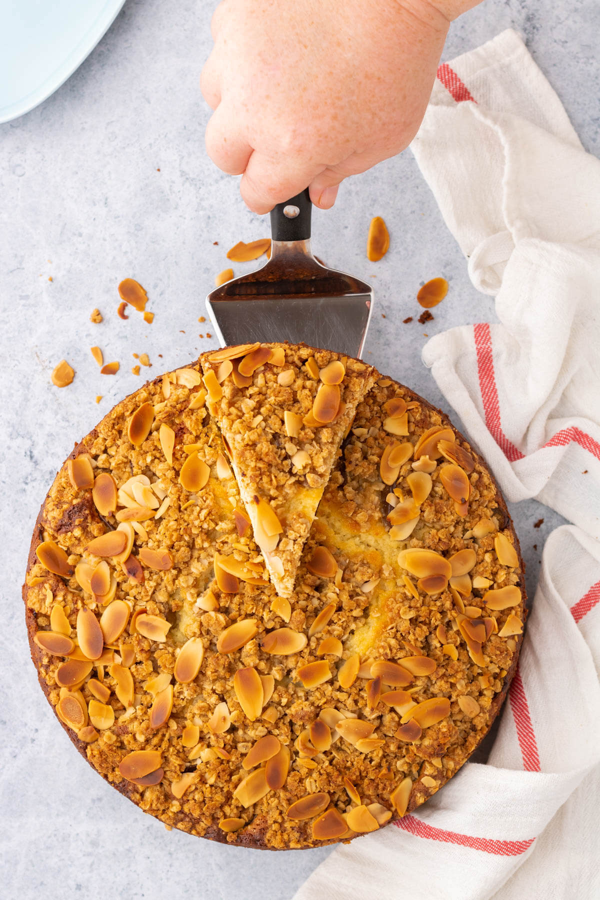 Overhead view of a golden almond crumble topped ricotta cake with a slice being served.