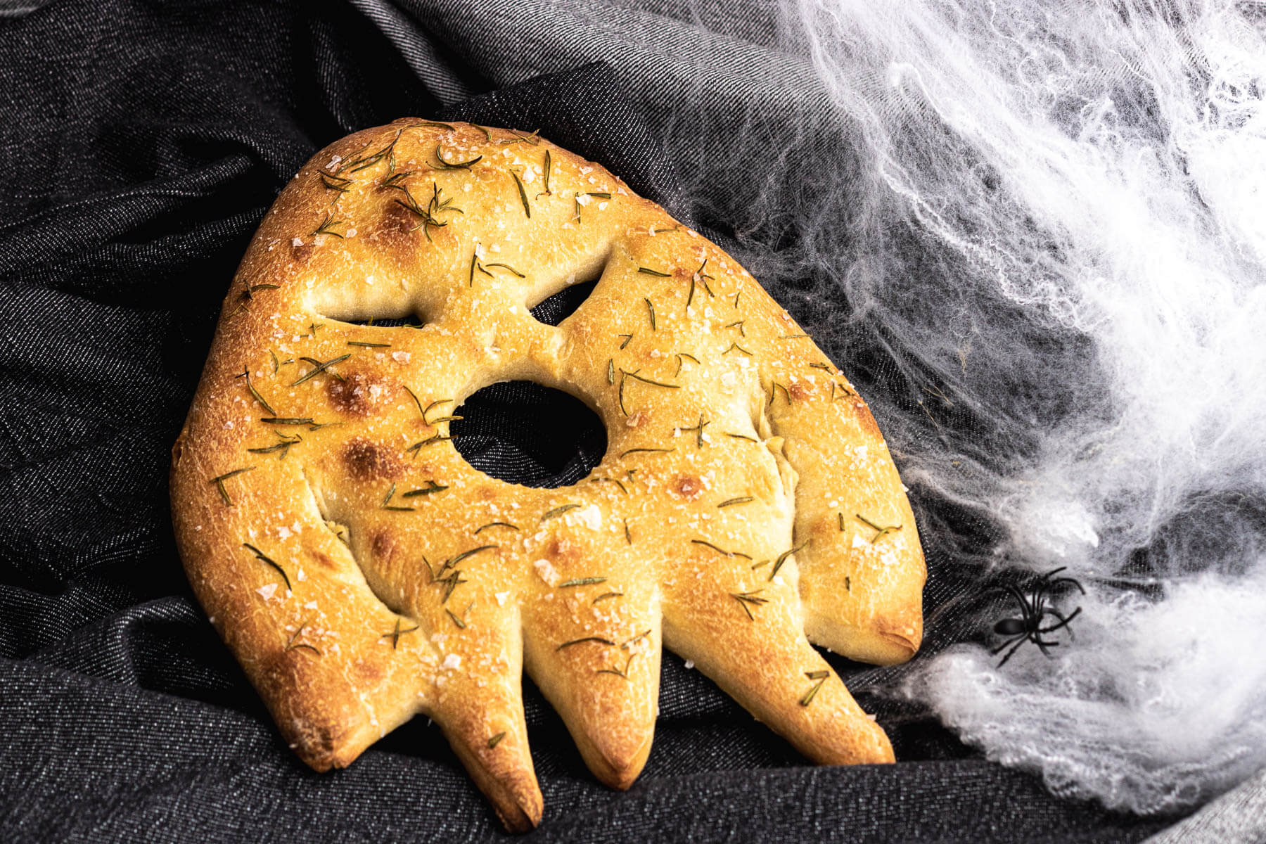 A ghost shaped baked fougasse flat bread on a dark background surrounded by spiderwebs..