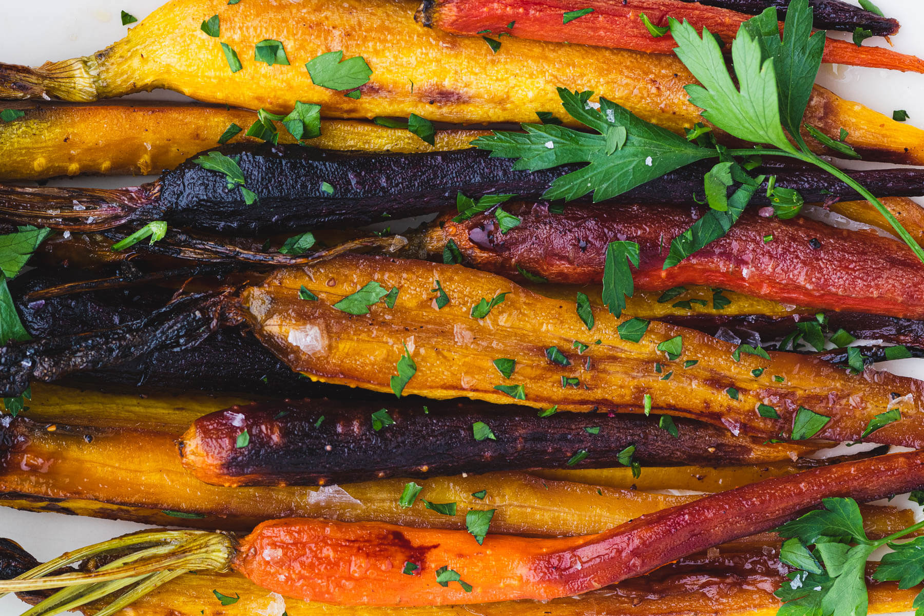 Colourful Maple Balsamic Roasted Carrots garnished with coarse salt and chopped parsley.
