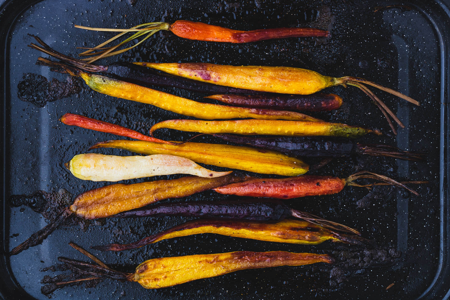 Colourful Maple Balsamic Roasted Carrots in a dark roasting pan.