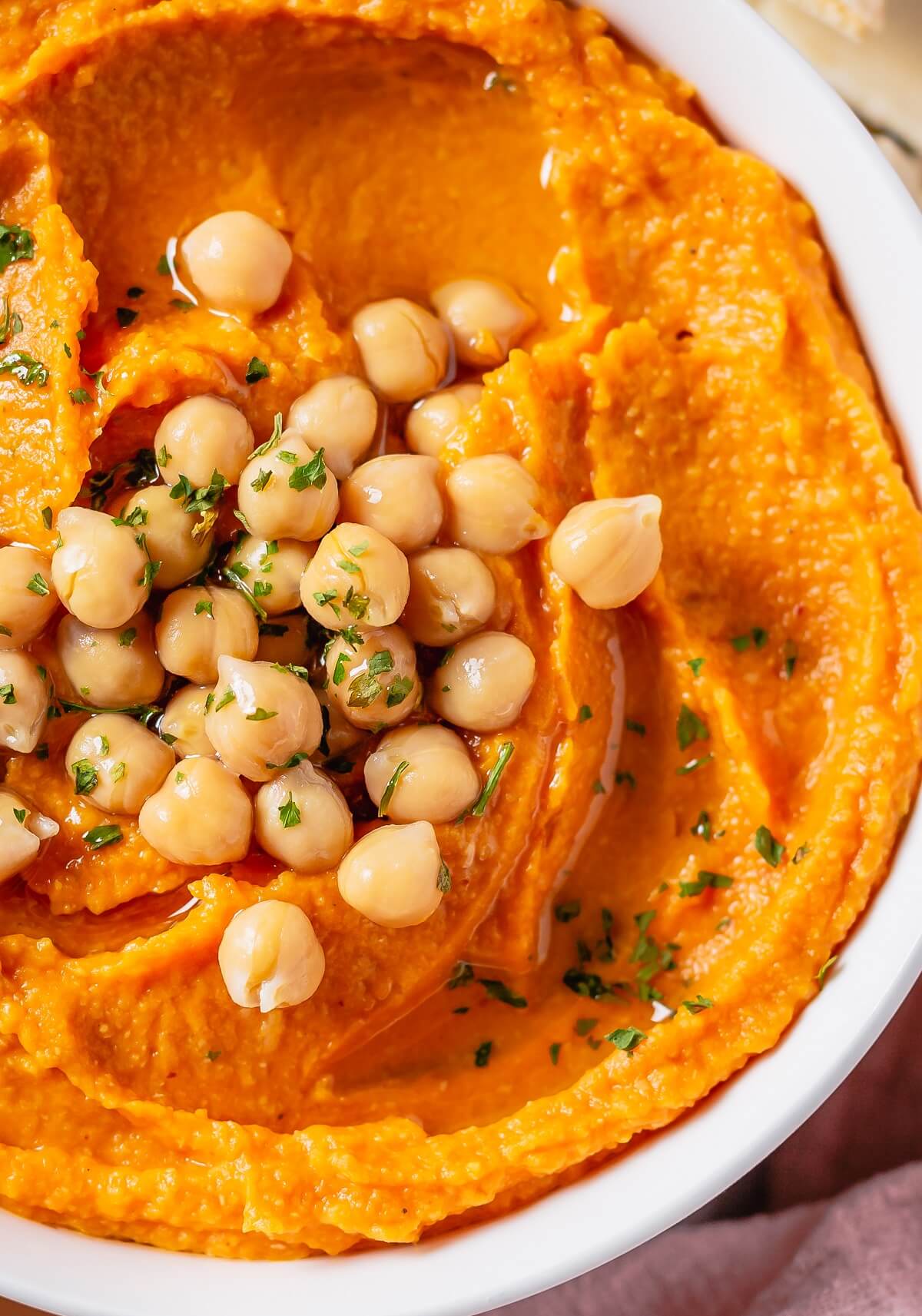 Close up of a bowl of pumpkin hummus garnished with chickpeas and olive oil.