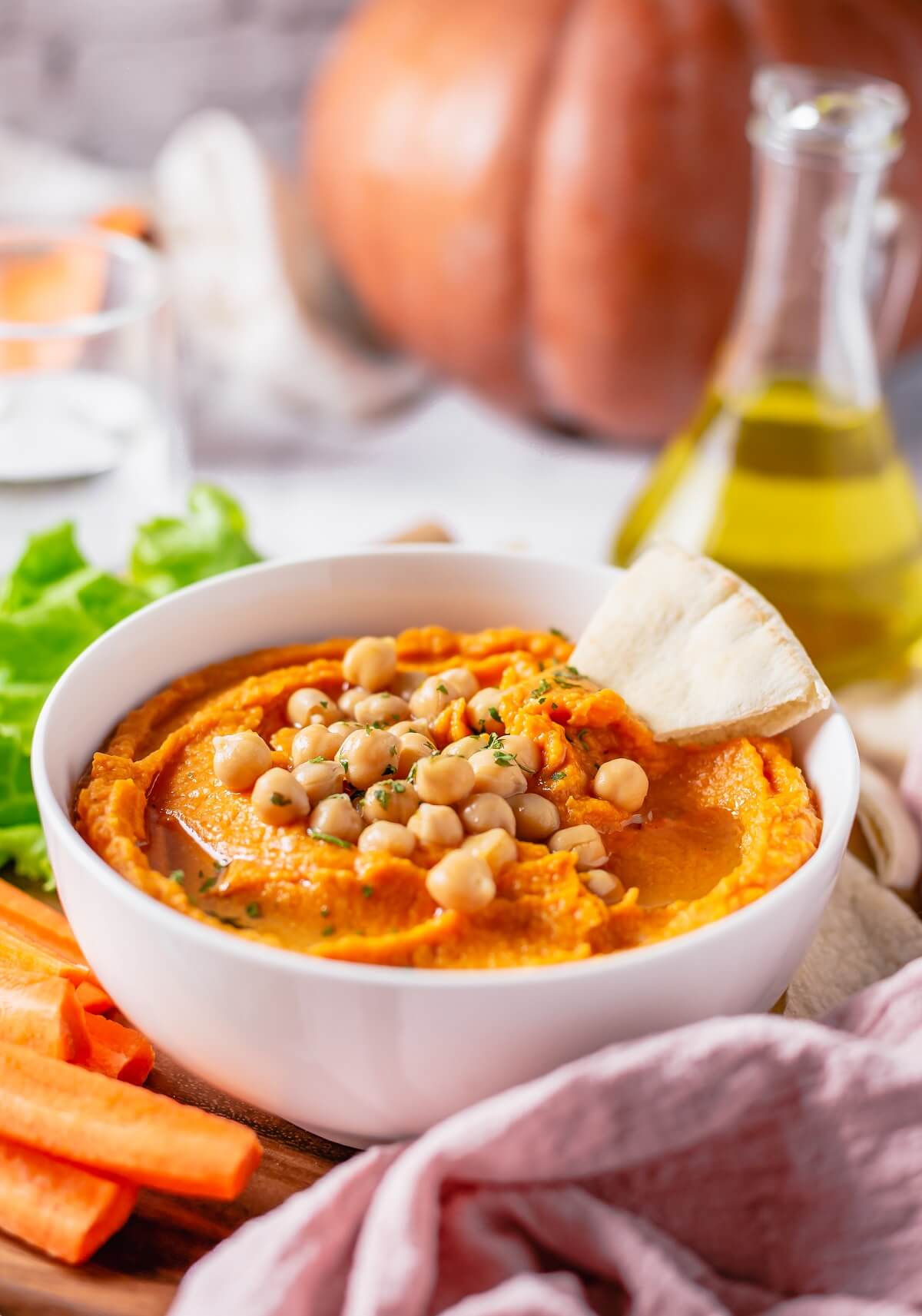 A white bowl of pumpkin hummus with a triangle of fresh pita in it.