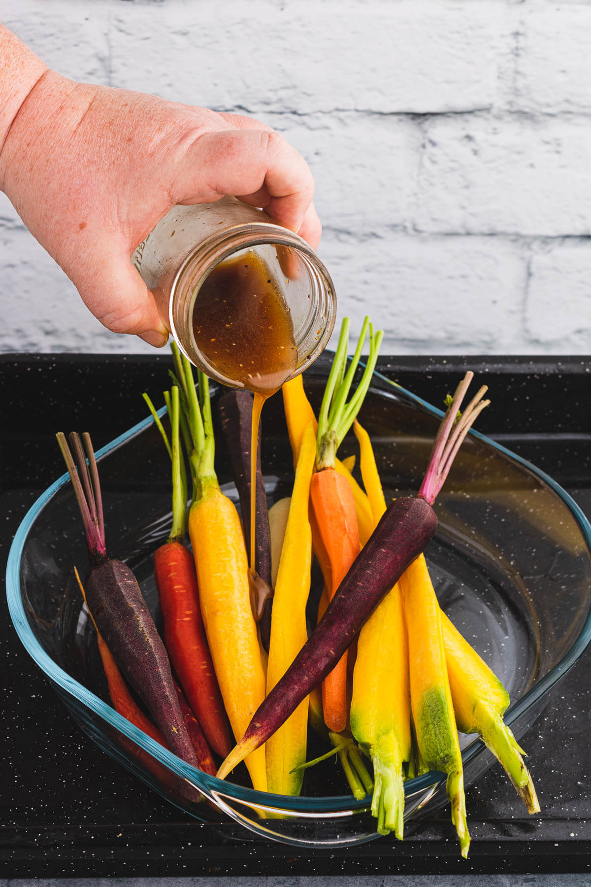 A variety of peeled colourful raw carrots being coated with maple balsamic vinaigrette before roasting.