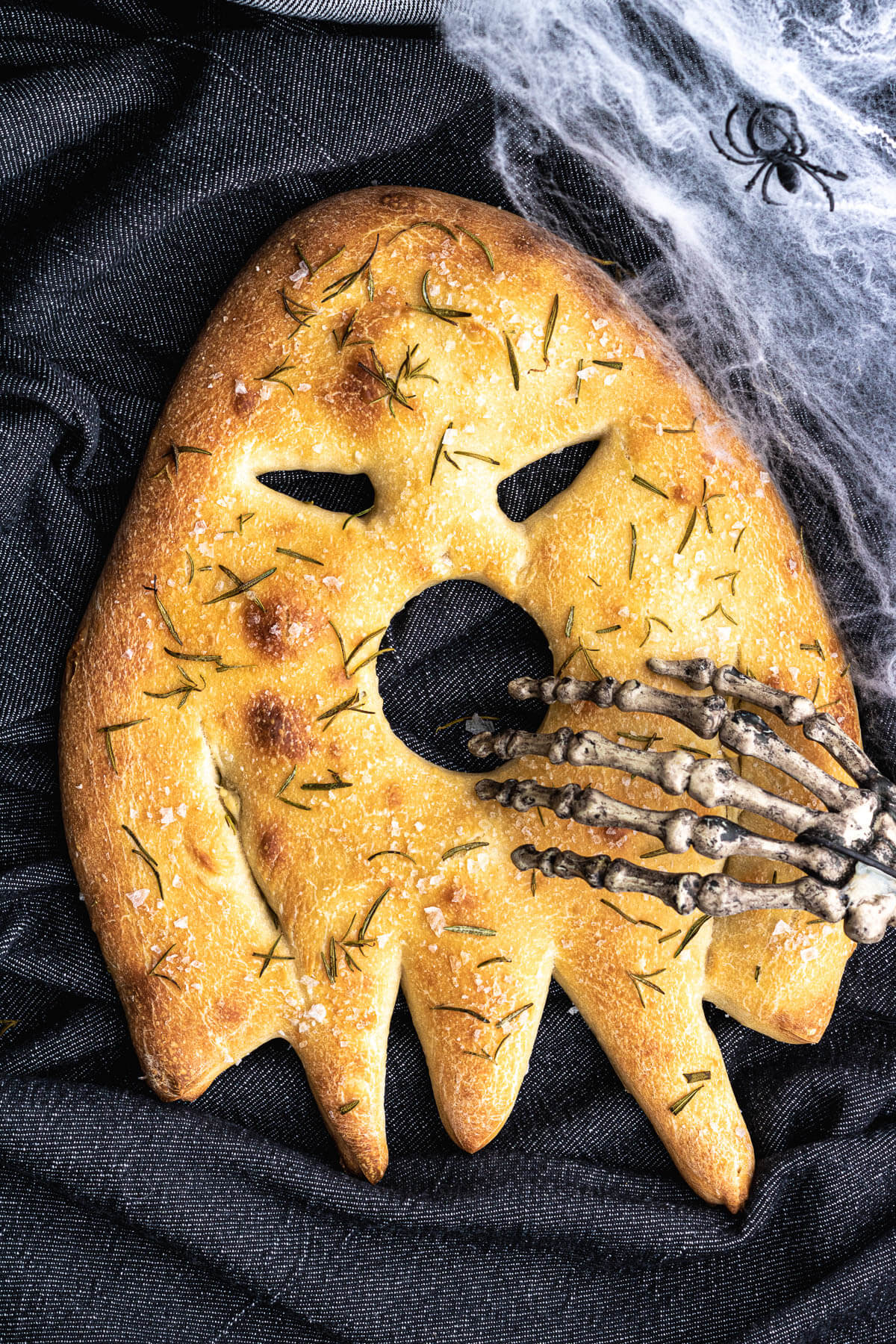 A ghost shaped sourdough fougasse flat bread with skeleton hand covering the open mouth.