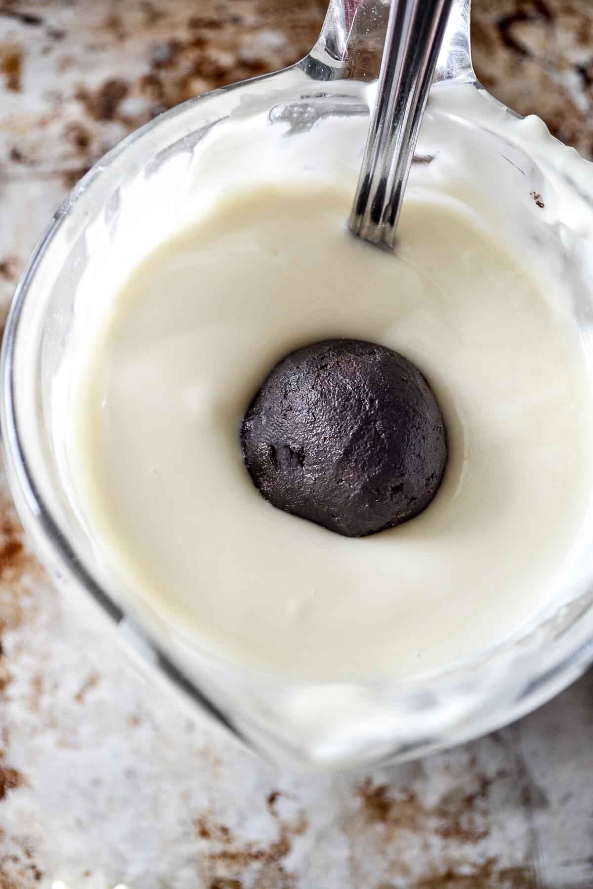 An oreo truffle ball being coated in melted white chocolate.