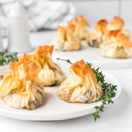 Golden baked Filo Pastry Parcels on a white serving plate garnished with fresh thyme.