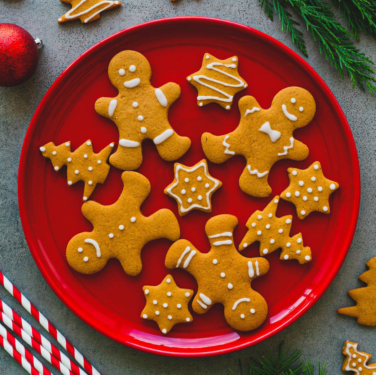 A red plate full of golden baked easy gingerbread cookies decorated with simple white piped icing embellishments.