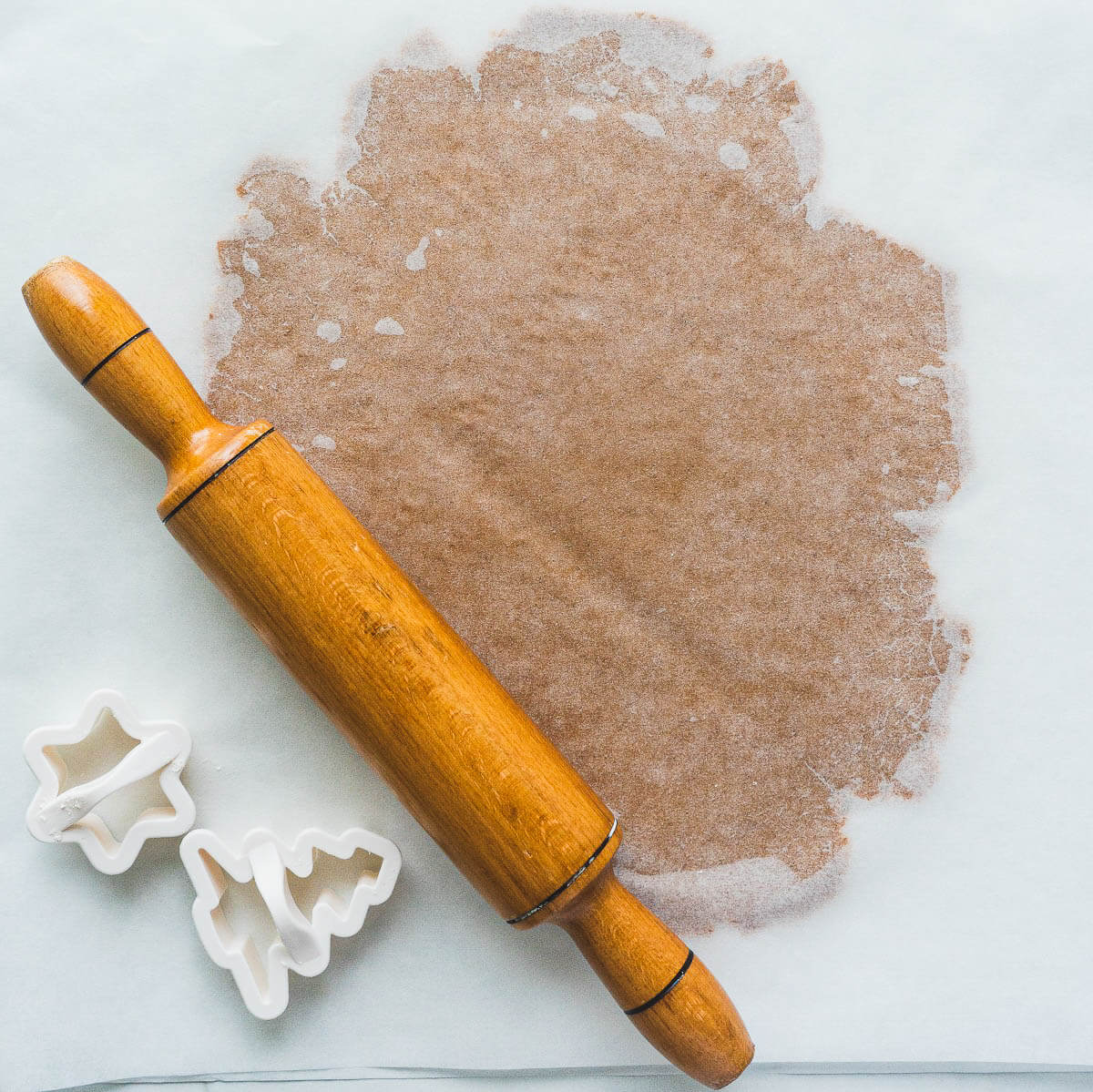 A wooden rolling pin beside rolled gingerbread cookie dough in between two pieces of parchment paper.