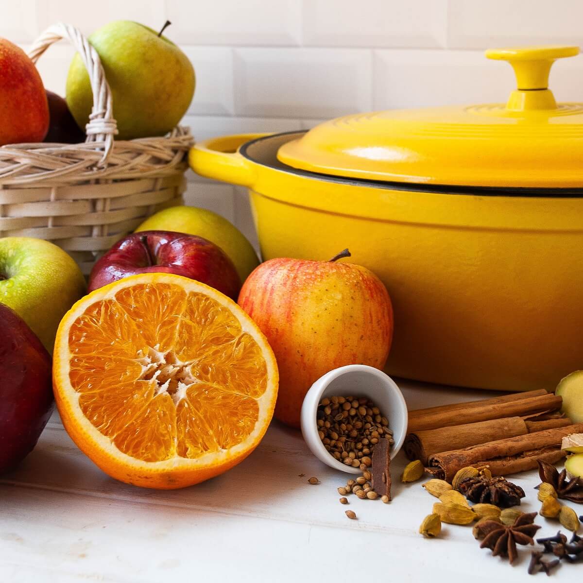 A yellow enamel Dutch oven surrounded by ingredients for hot apple cider.