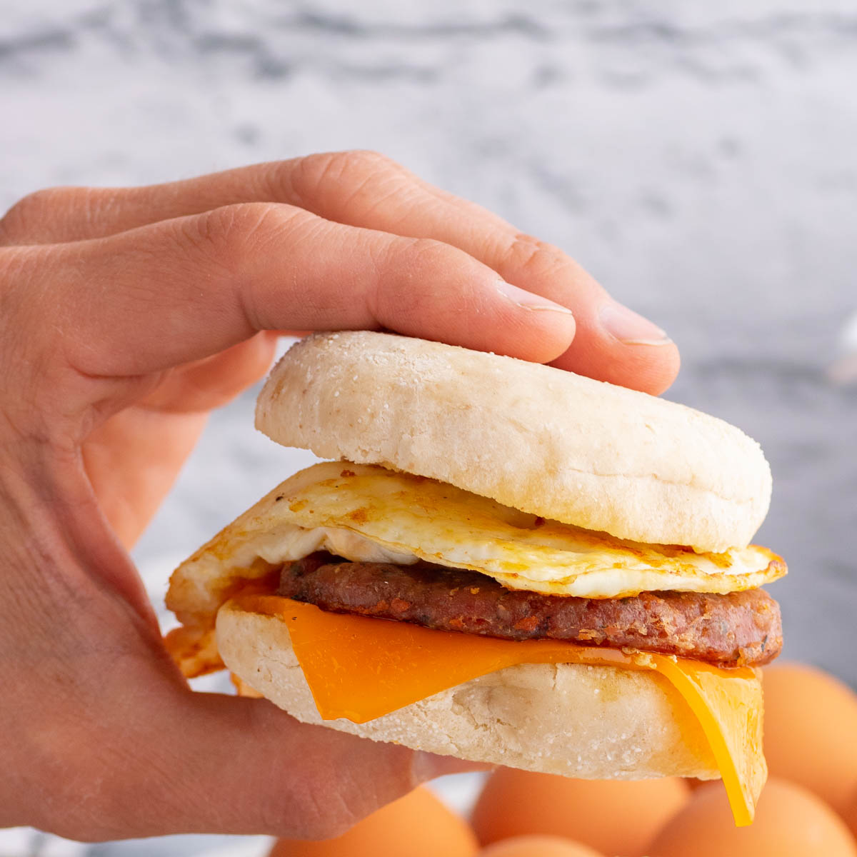 A hand holds an egg and sausage breakfast sandwich.