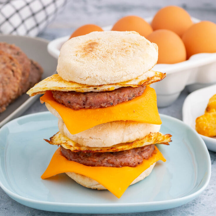 A stack of English muffin breakfast sandwiches surrounded by the ingredients used to make them.