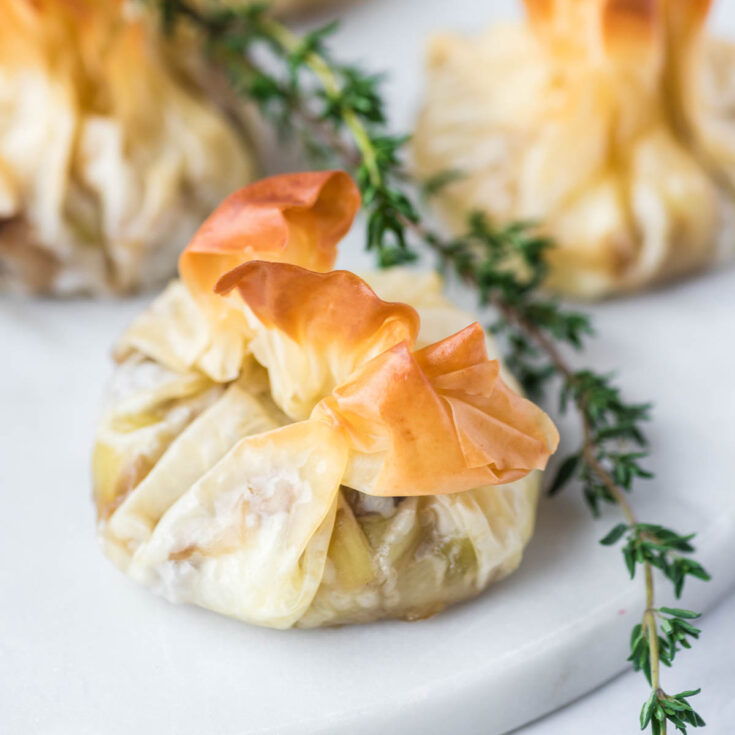 Golden baked Filo Pastry Parcels on a white serving plate garnished with fresh thyme.