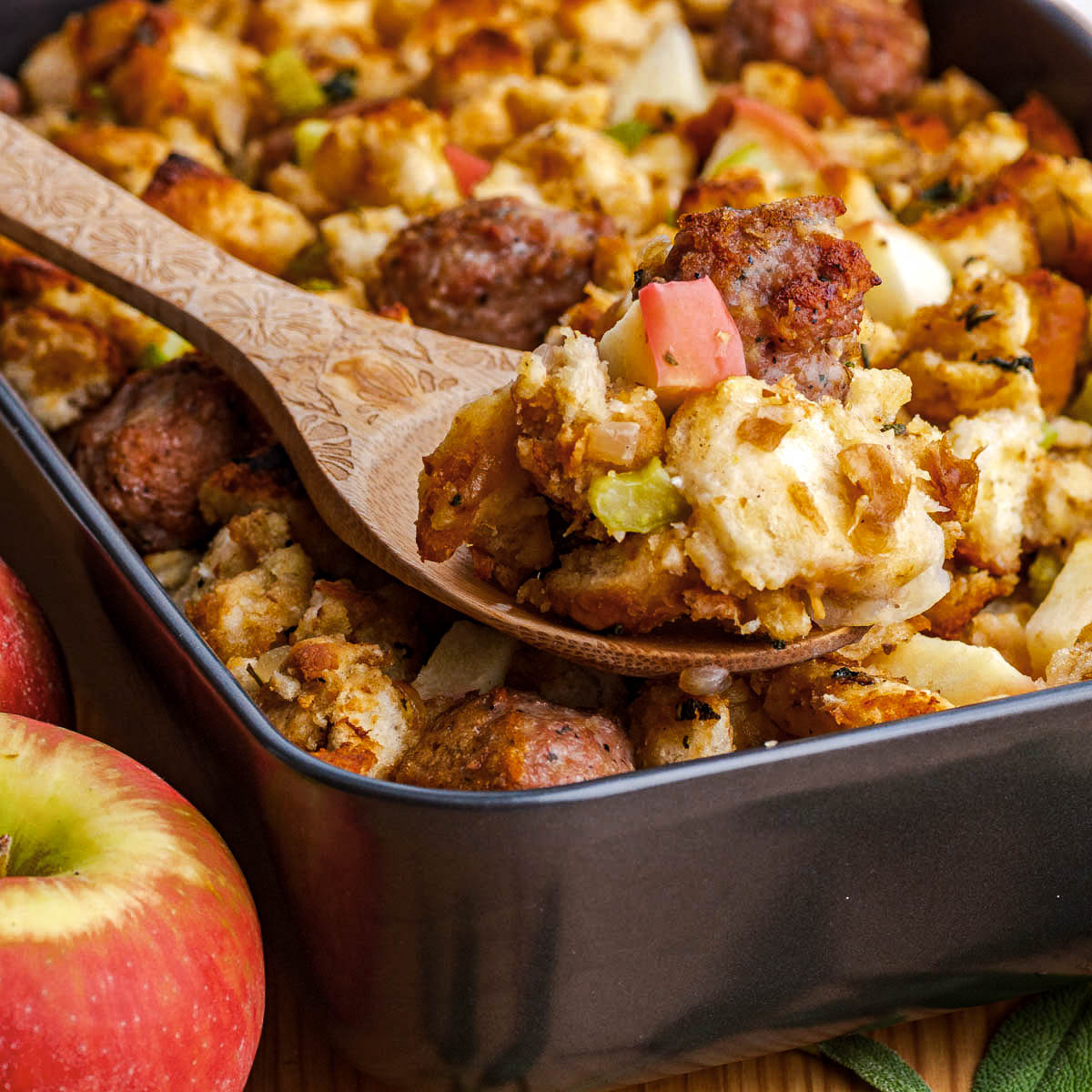A wooden spoon sit in a pan of Apple Sausage Stuffing.