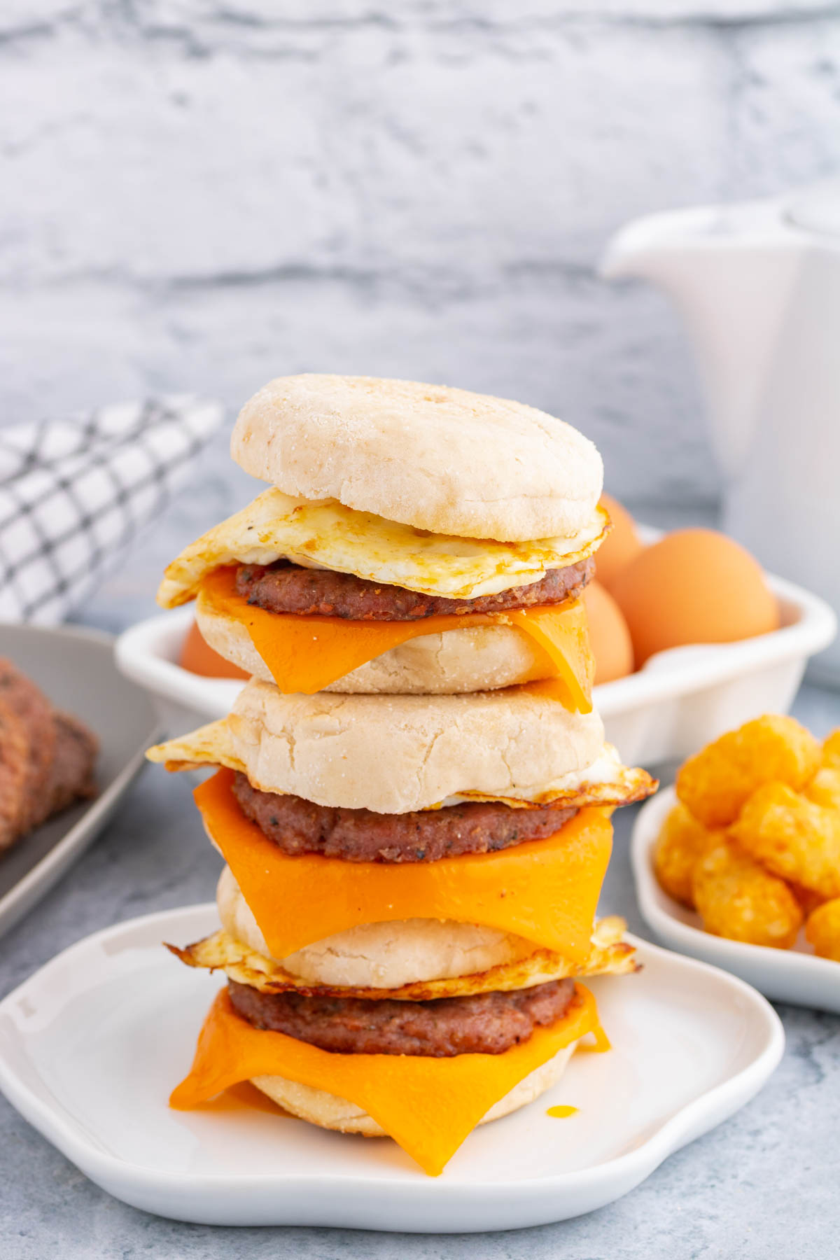A stack of English muffin breakfast sandwiches surrounded by the ingredients used to make them.