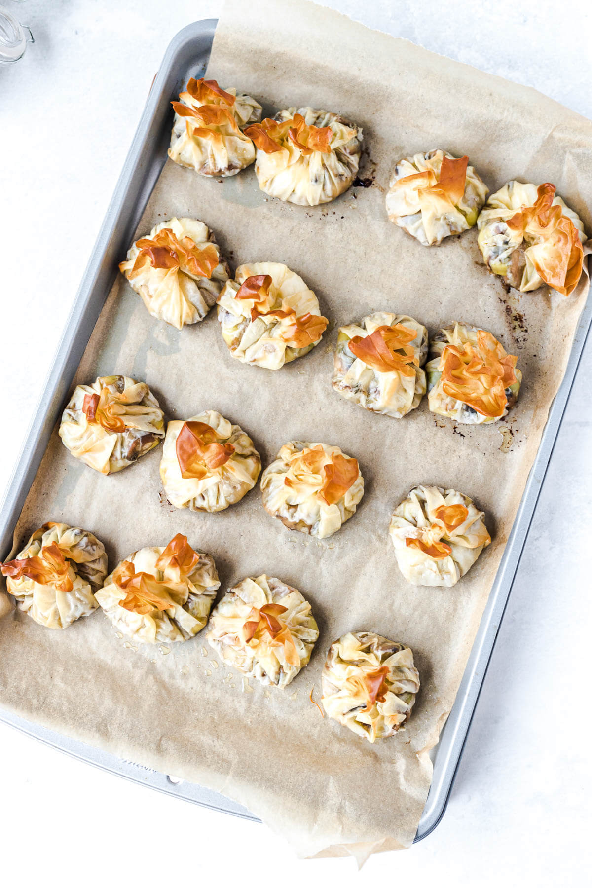 A baking sheet filled with golden baked mushroom goat cheese filo pastry parcels.