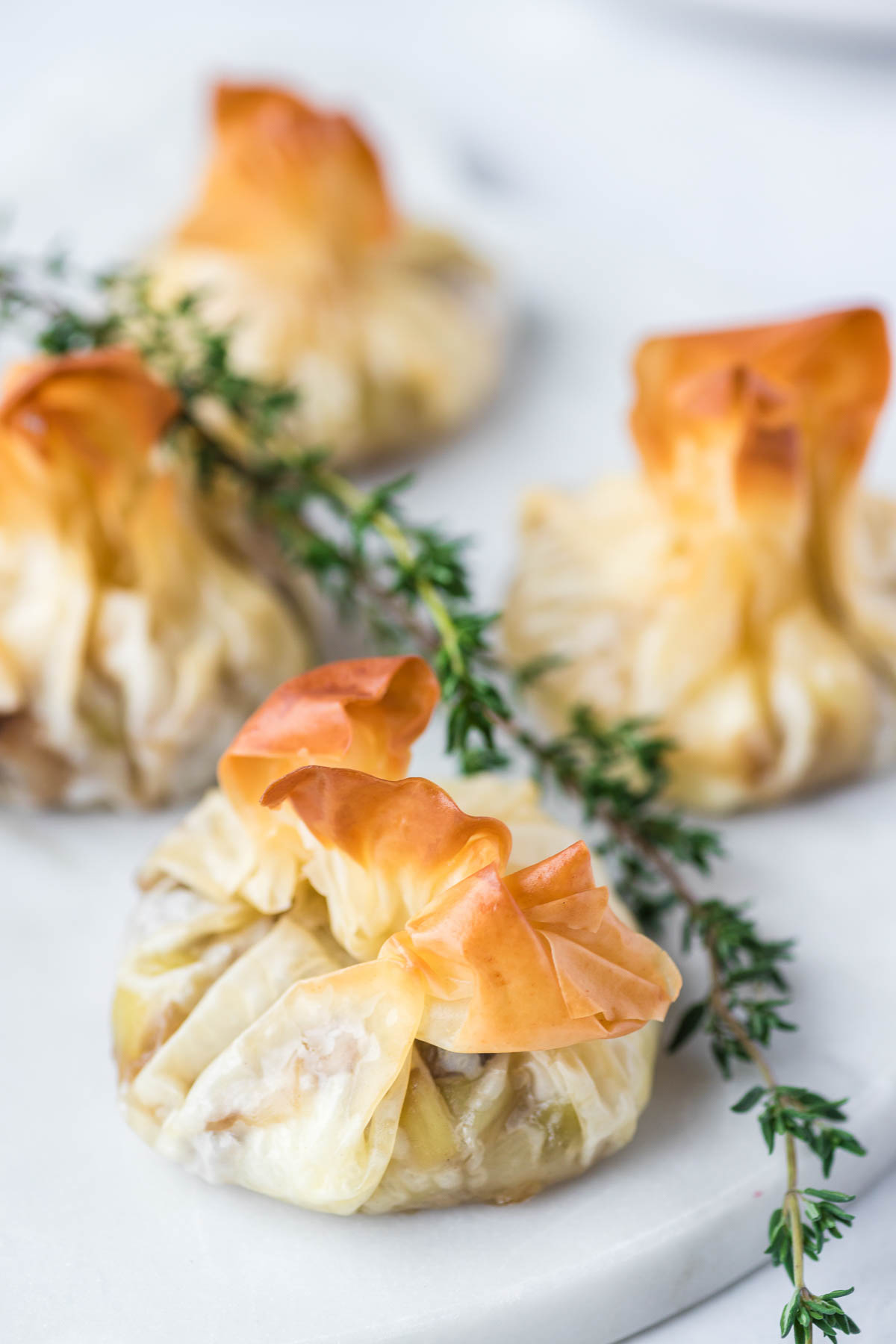 Golden baked Filo Pastry Parcels on a white serving plate garnished with fresh thyme. 