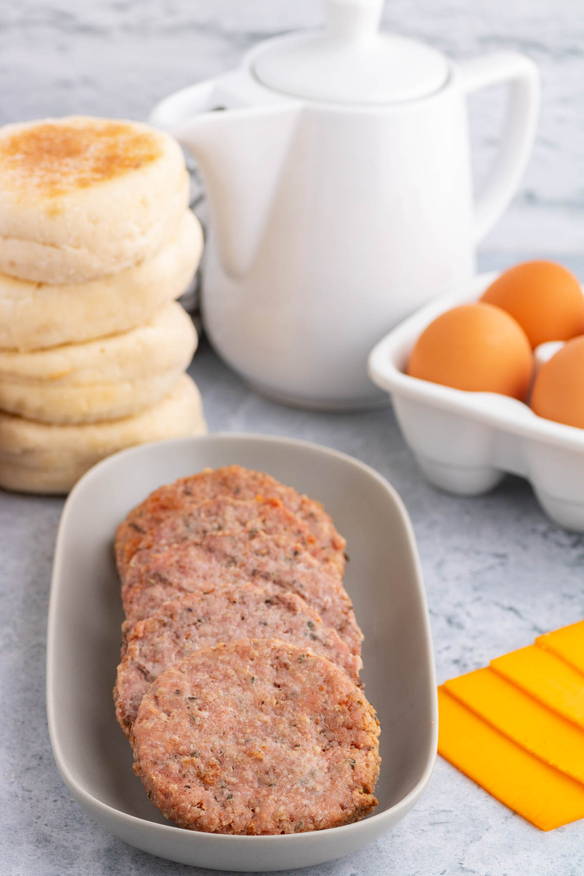 A tray of smoked breakfast sausage patties surrounded by the ingredients for breakfast sandwiches.