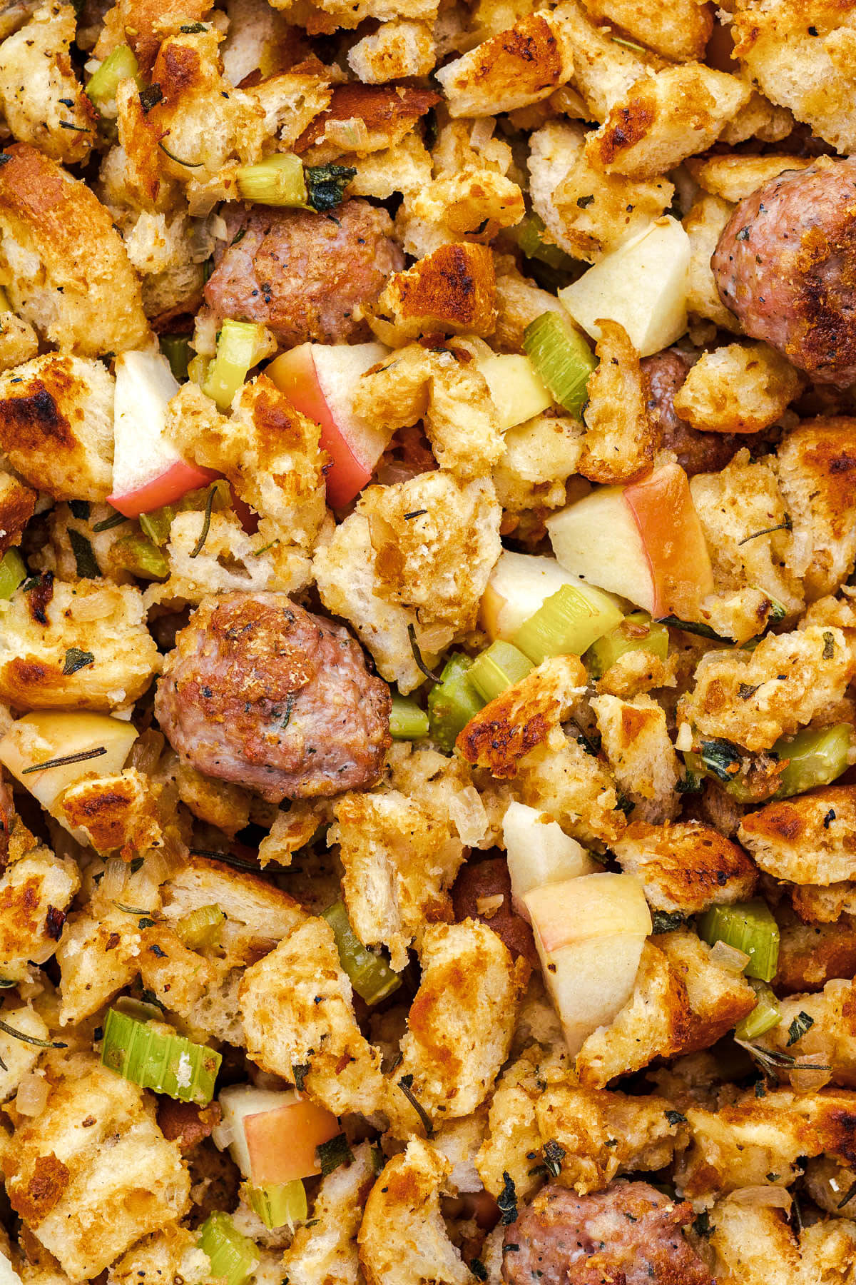 A close view of golden baked chunky bread crumbs, cooked sausage, apples, and celery garnished with fresh herbs.