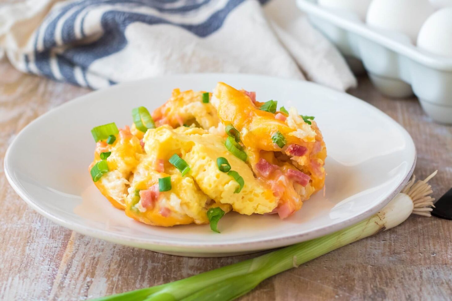 A serving of slow cooker breakfast casserole with ham, cheddar cheese, and green onions served on a white plate on a breakfast table.
