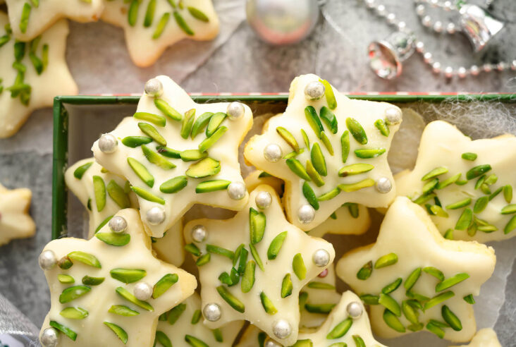 Close up of sugar star cookies decorated with pistachios and silver dragées.